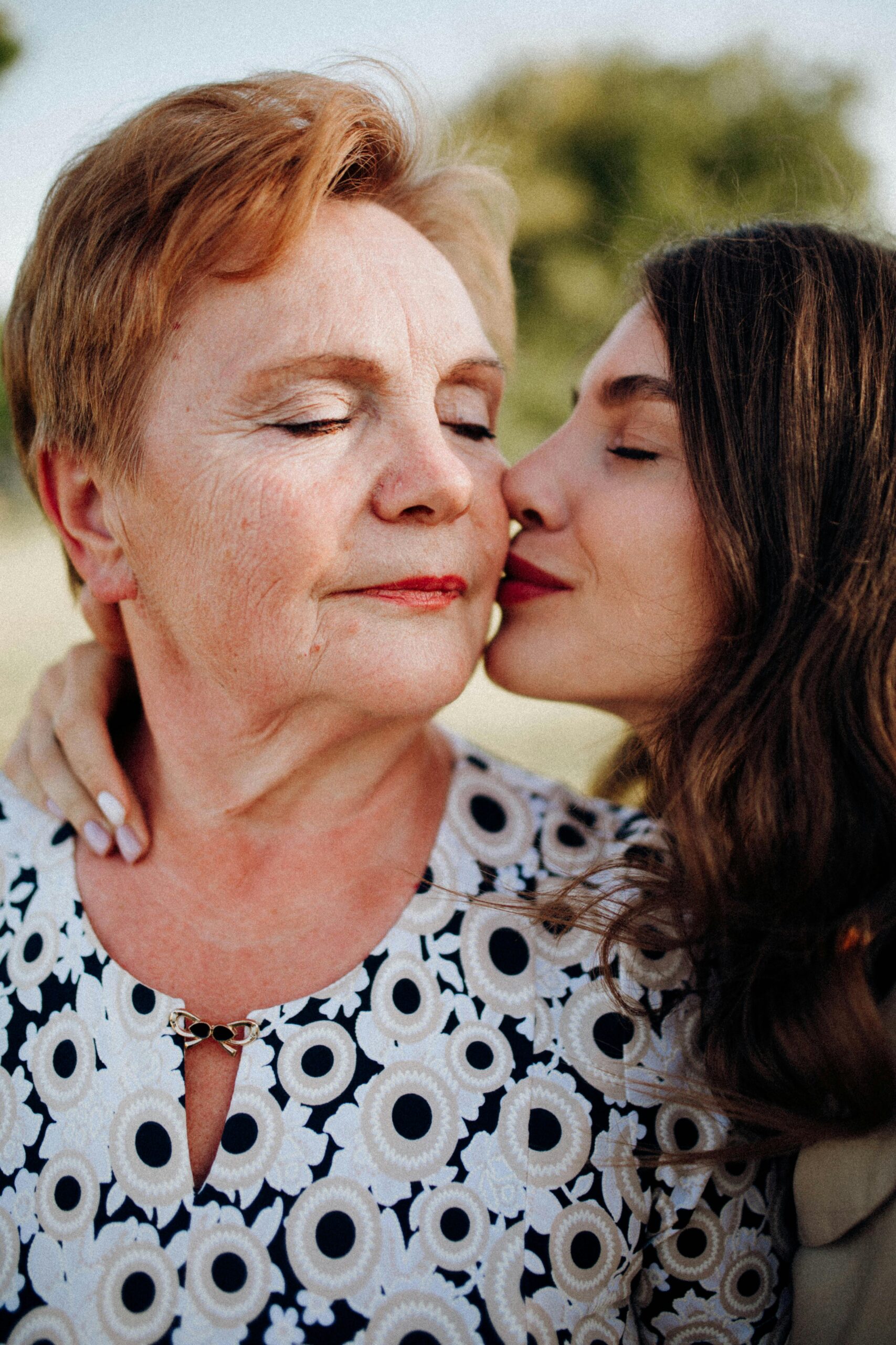 A tender moment of a woman kissing her mother on the cheek outdoors, symbolizing love and connection.